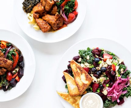 Spread of plates with greens, fruit and meat at Three Carrots