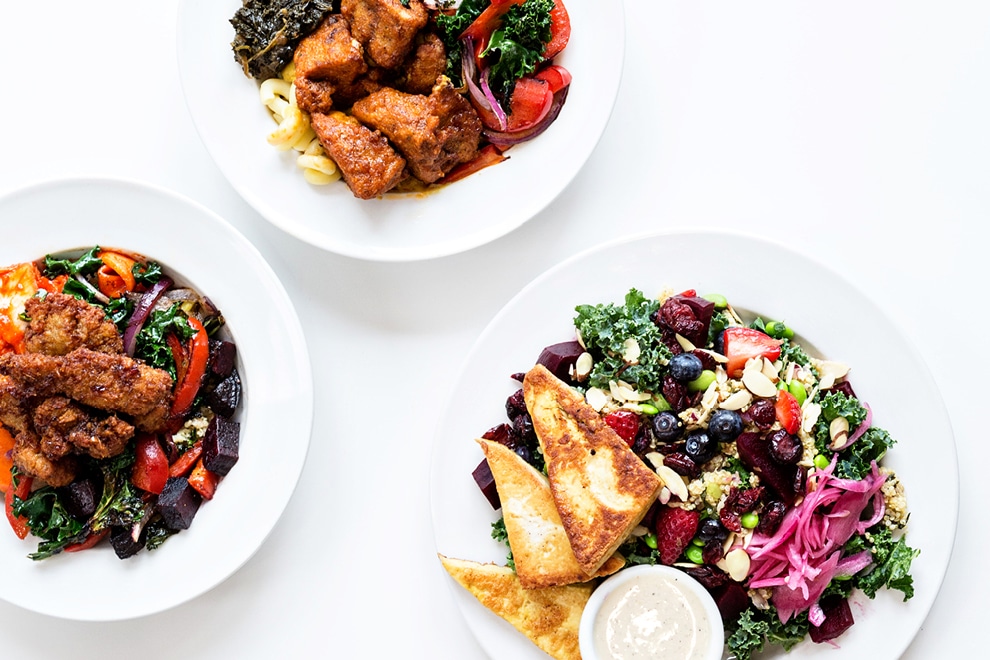 Spread of plates with greens, fruit and meat at Three Carrots