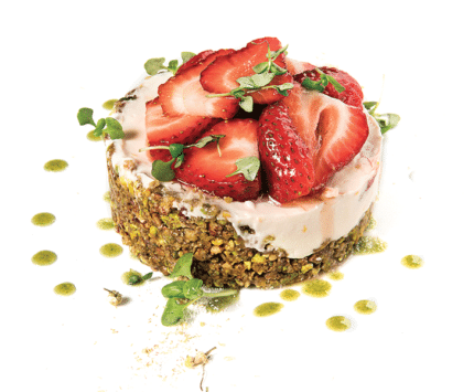 A pink cheesecake topped with red strawberry slices and micro-basil.