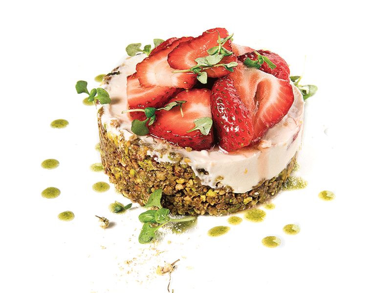 A pink cheesecake topped with red strawberry slices and micro-basil.