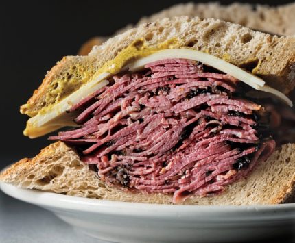 A sandwich stacked high with corned beef, Swiss cheese, and yellow mustard on rye