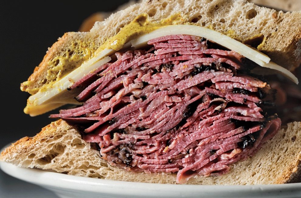 A sandwich stacked high with corned beef, Swiss cheese, and yellow mustard on rye