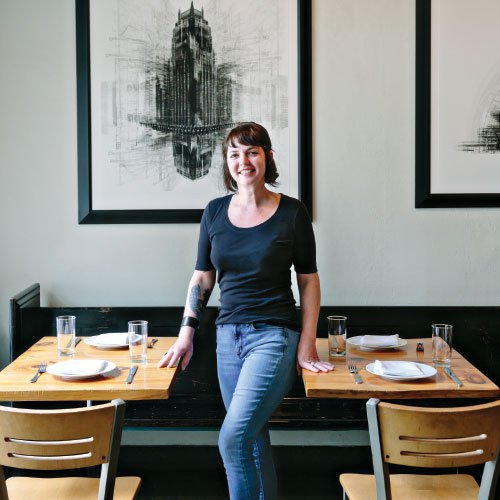 A woman stands between two dining tables of a restaurant.