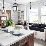 A white kitchen with subway tile, marble countertops, and dark island cabinets.