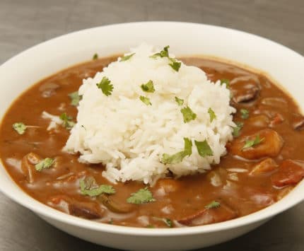 A hearty bowl of gumbo topped with a spoonful of white rice.