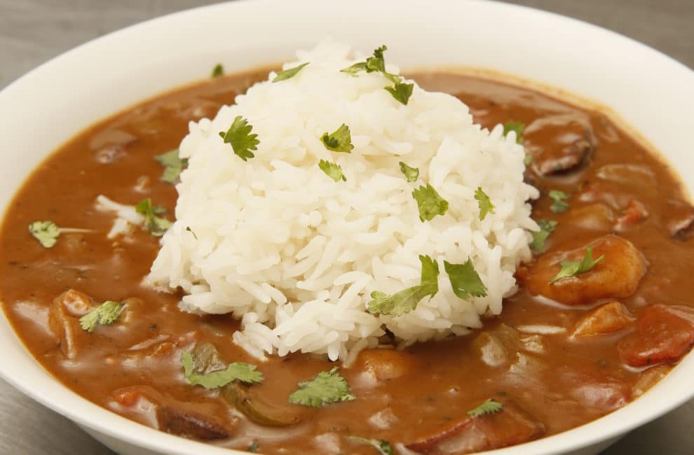 A hearty bowl of gumbo topped with a spoonful of white rice.