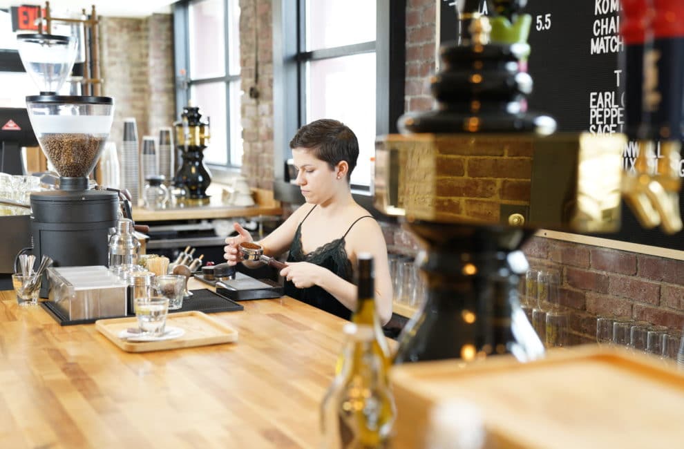 A woman prepares coffee behind the high wooden counter at a barbershop.