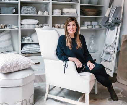 A woman sits in an oversized white chair surrounded by interior design products.