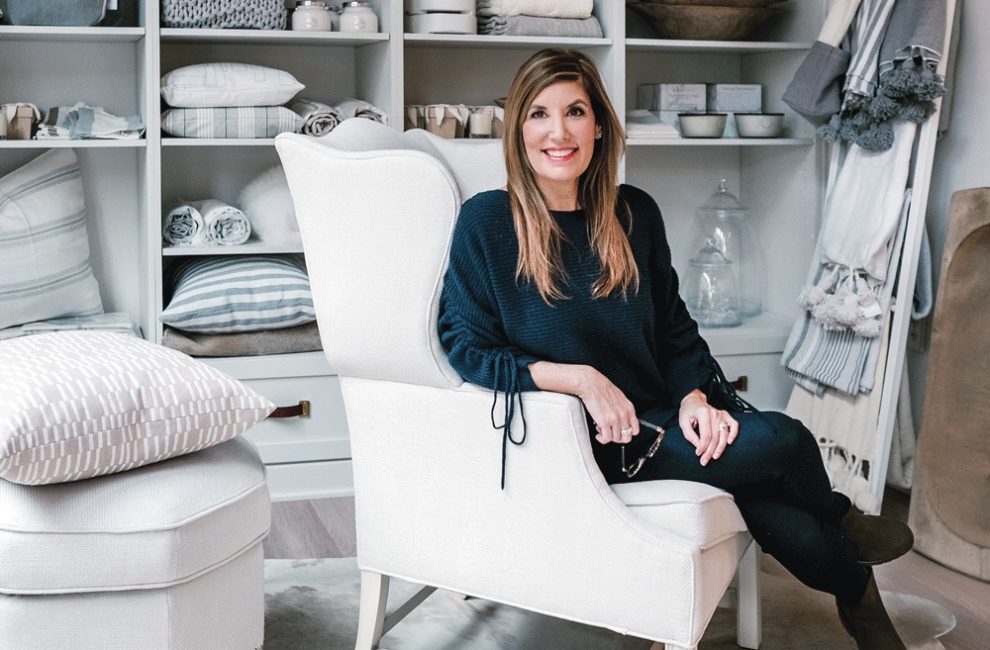 A woman sits in an oversized white chair surrounded by interior design products.