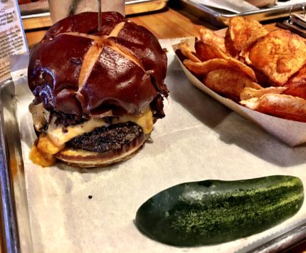 A sheet pan lined with white sandwich paper with a cheeseburger and green pickle spear.