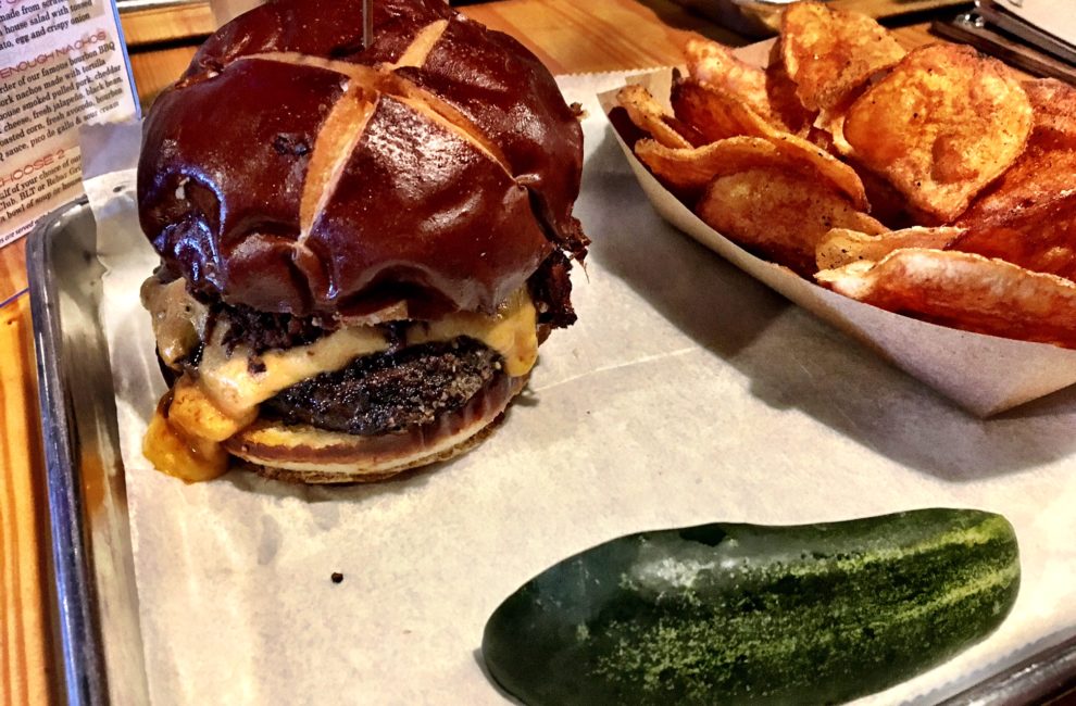 A sheet pan lined with white sandwich paper with a cheeseburger and green pickle spear.