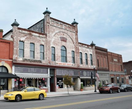 A downtown streetscape featuring a bricked two-story building.