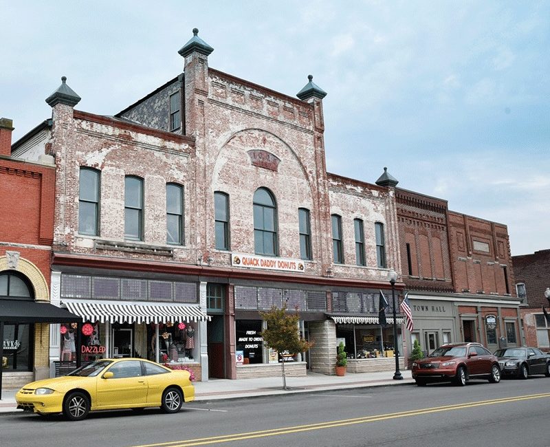 A downtown streetscape featuring a bricked two-story building.