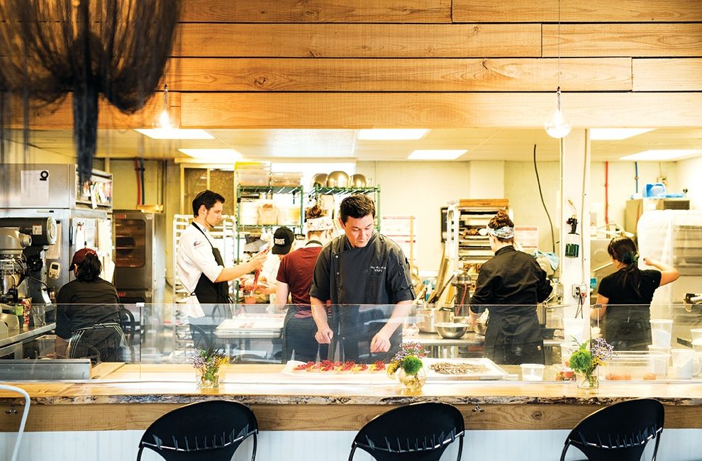 A gentleman wearing an apron works in a busy pastry kitchen.