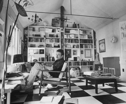 Black and white image of Kurt Vonnegut sitting in a chair inside an office.