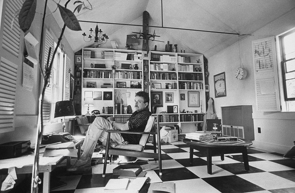 Black and white image of Kurt Vonnegut sitting in a chair inside an office.