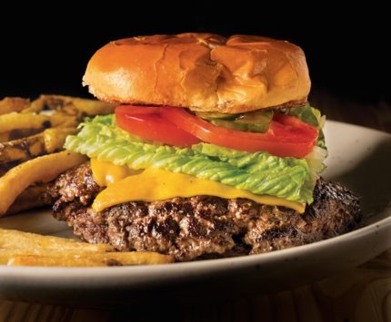 A double stacked cheeseburger with crisp lettuce, tomatoes, and pickles sits on a plate of fries.