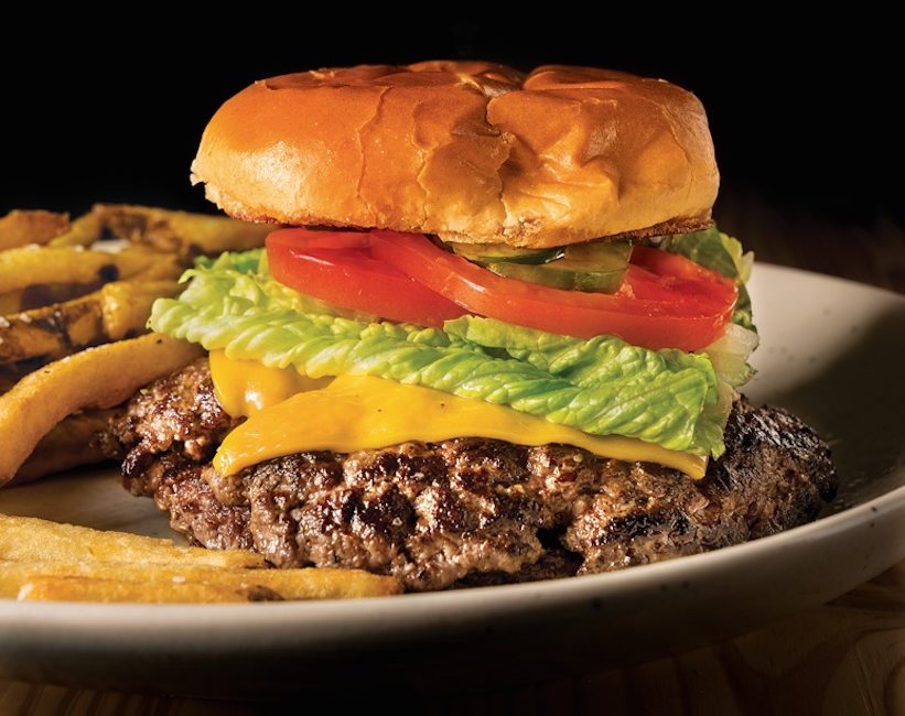 A double stacked cheeseburger with crisp lettuce, tomatoes, and pickles sits on a plate of fries.