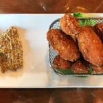 A white rectangular plate holds brown grain mustard and a basket of cheese curds.