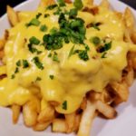 A mammoth plate of a crispy French fries topped with cheese sauce.