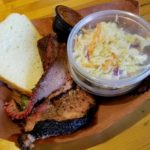 A wide brown paper bowl holds smoked brisket, sides, and a slice of white bread.