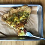 A silver tray holds a giant slice of green pesto queiche.