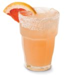 A grapefruit hued drink in a tall tumbler with a sugar rimmed garnish