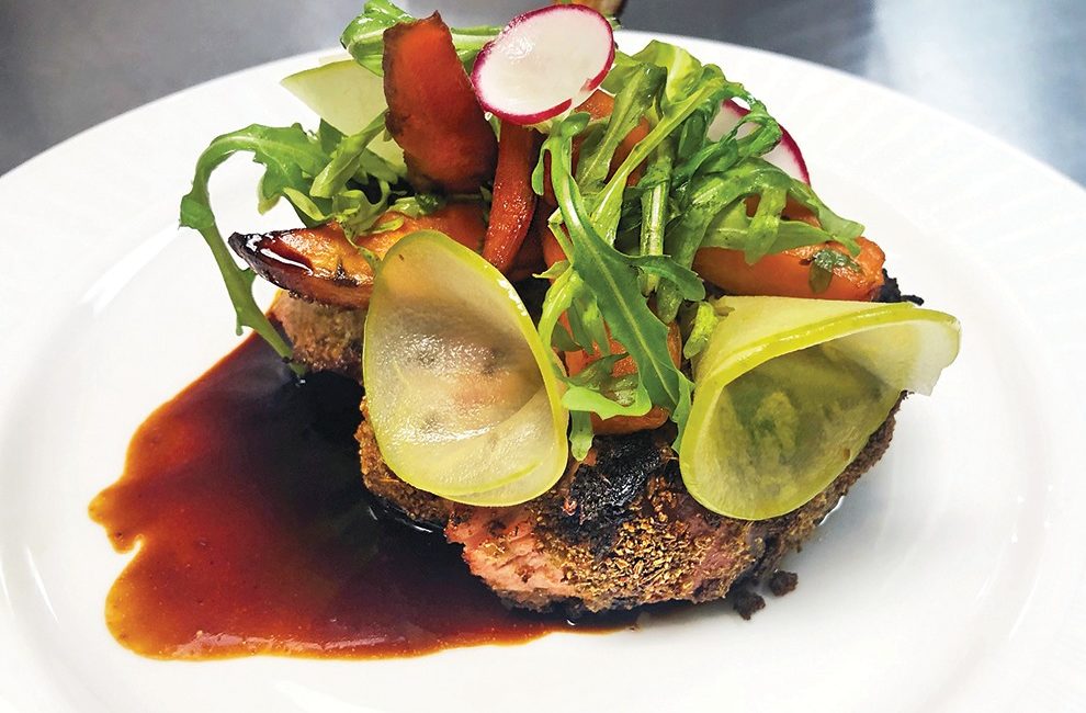 A colorful plate of food that includes roasted carrots, sliced raddish, and pickles.