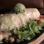 A stuffed burrito topped with quso and guacamole