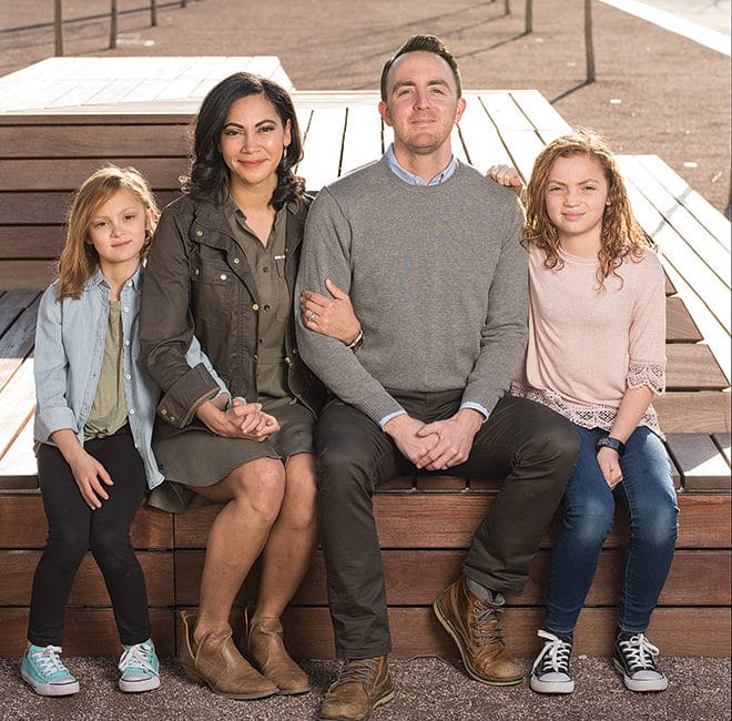 A family of four sits on a park bench.