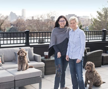 Two women pose with their dogs on a downtown terrace.