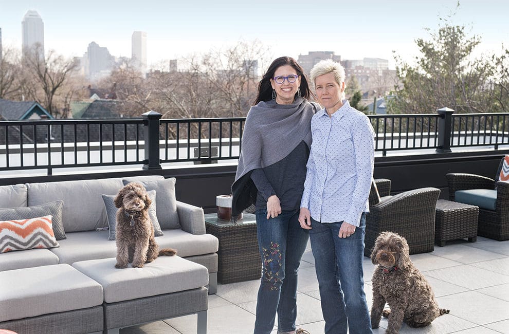 Two women pose with their dogs on a downtown terrace.