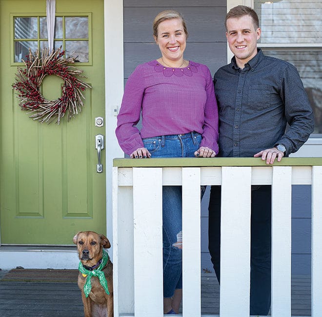 A woman and a man stand on the front porch of a house.