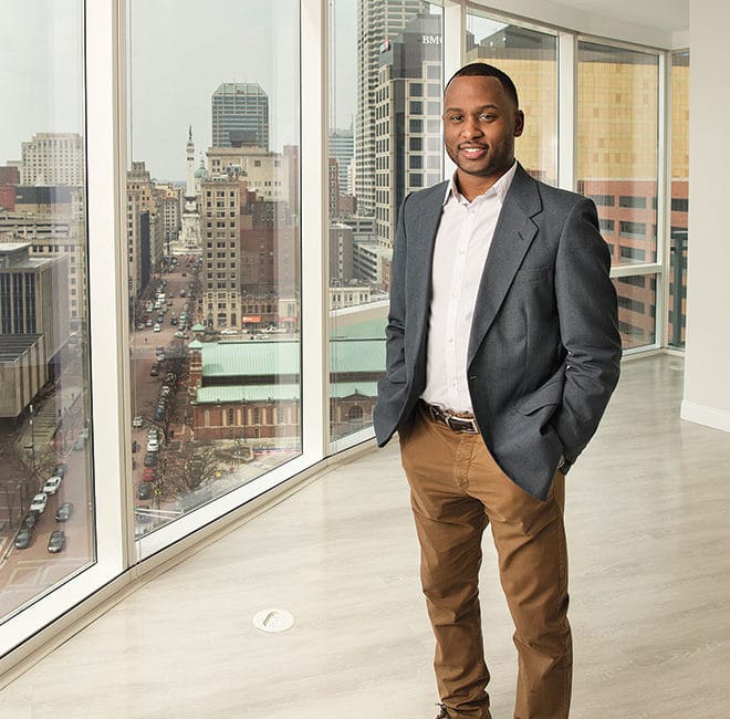 A gentleman stands in a glass-walled urban apartment.