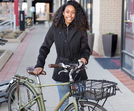 A woman stands behind a bicycle outside of an urban apartment building.