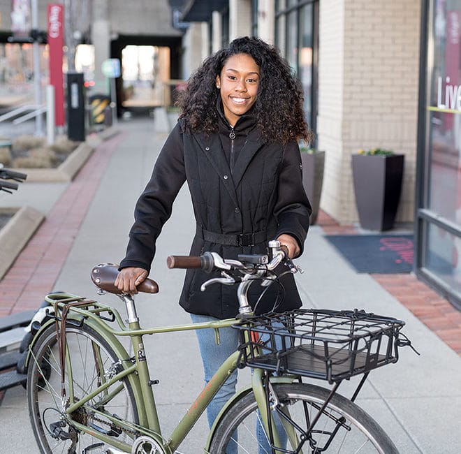 A woman stands behind a bicycle outside of an urban apartment building.