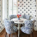 A small white circular dining table with plush, oversized chairs adorned in paisley fabric.