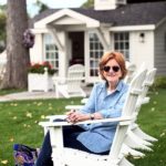 A woman dons sunglasses while sitting in a white Adorondack chair.