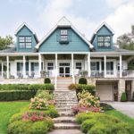 A large, blue lake house with a wraparound porch.