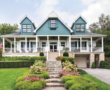 A large, blue lake house with a wraparound porch.