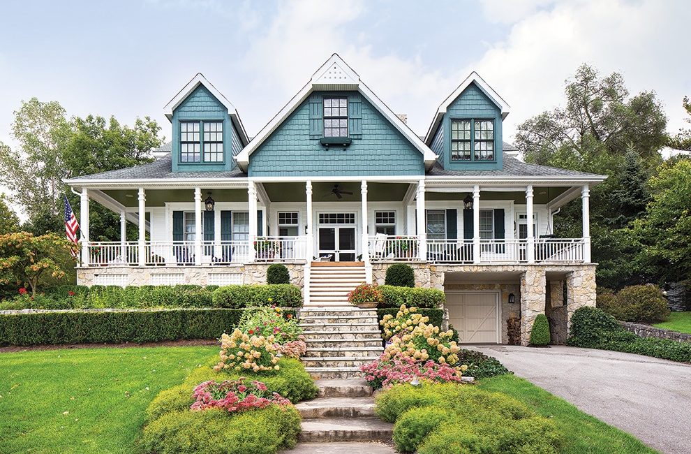 A large, blue lake house with a wraparound porch.