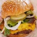 A cheeseburger topped with fixings squeezed between a sesame seed bun.