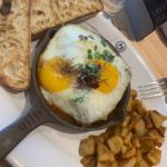 A skillet of eggs and meatballs with a side of roasted potatoes and toast.