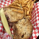 A basket of a sandwich, fries, and pickle spear.