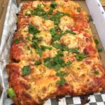 A square pizza with seafood and cheese topped with fresh parsley and green onions.