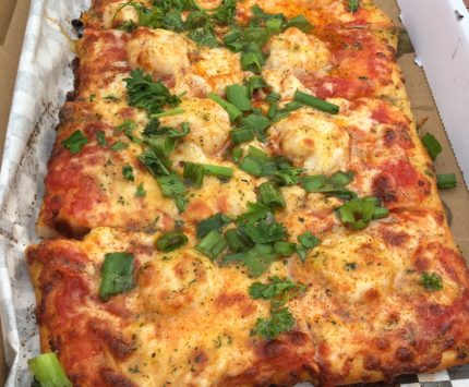 A square pizza with seafood and cheese topped with fresh parsley and green onions.