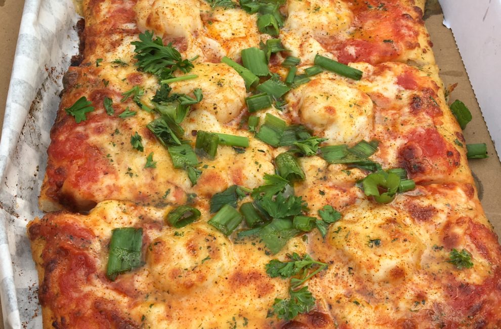 A square pizza with seafood and cheese topped with fresh parsley and green onions.