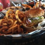 Buttery burger buns hold together a gooey cheeseburger topped with fixings with a side of curly fries.