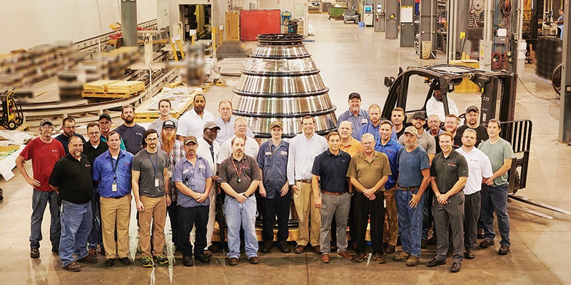 Men stand on a factory floor.