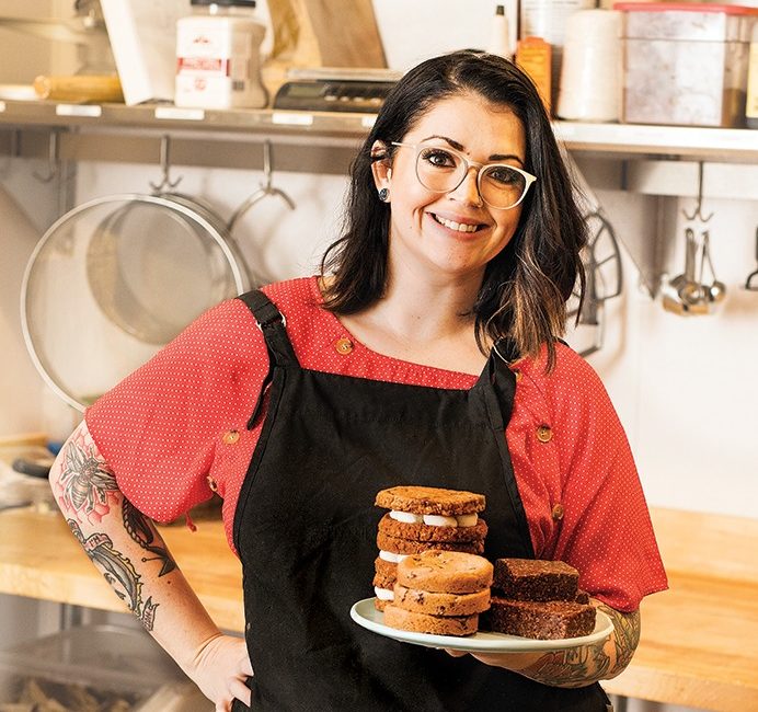 A woman dons a black apron while holding a plate of pastries.